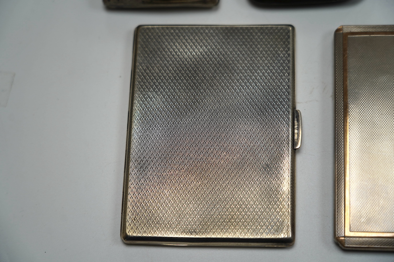 A George VI engine turned silver cigarette case, with yellow metal band, London, 1938, 11.4cm, four other silver cigarette cases and a silver ashtray, gross weight 16.8oz. Condition - poor to fair